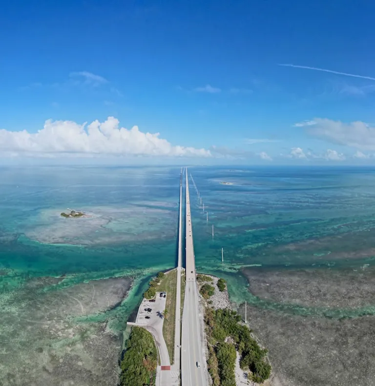 Aerial view of a long bridge over turquoise ocean waters under a clear blue sky.