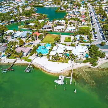 Aerial view of a coastal residential neighborhood with houses, docks, green lawns, and turquoise water.