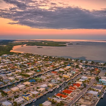 Aerial view of a coastal town with canals, houses, and a sunset sky with clouds.