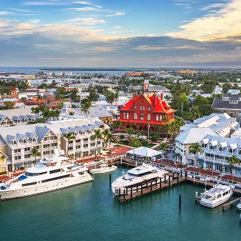 Aerial view of a coastal marina with boats, white buildings, and a prominent red-roofed historic building.