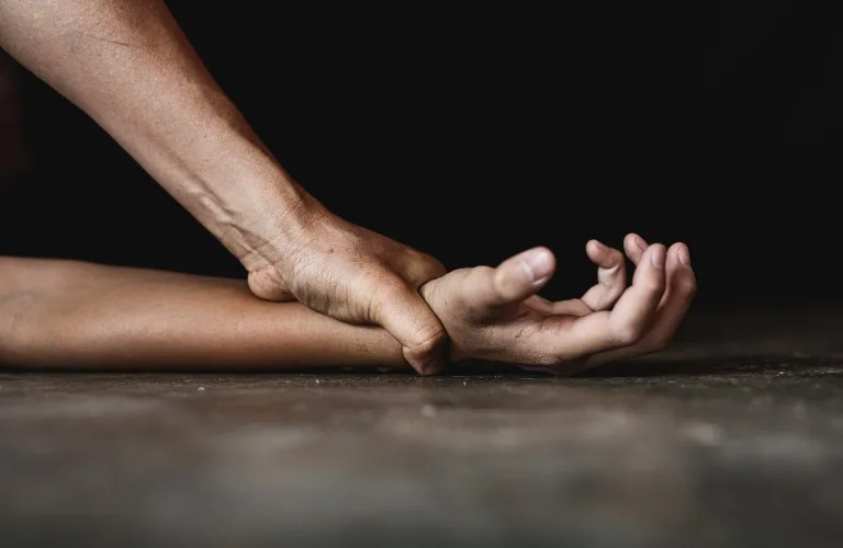 Two hands gripping a wrist firmly against a dark background, close-up view.