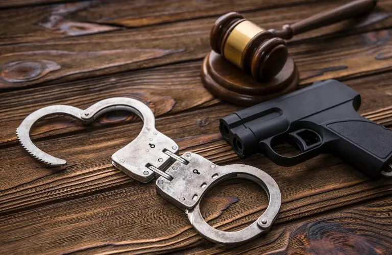 Metal handcuffs shaped like a heart, a black handgun, and a wooden gavel on a wooden surface.