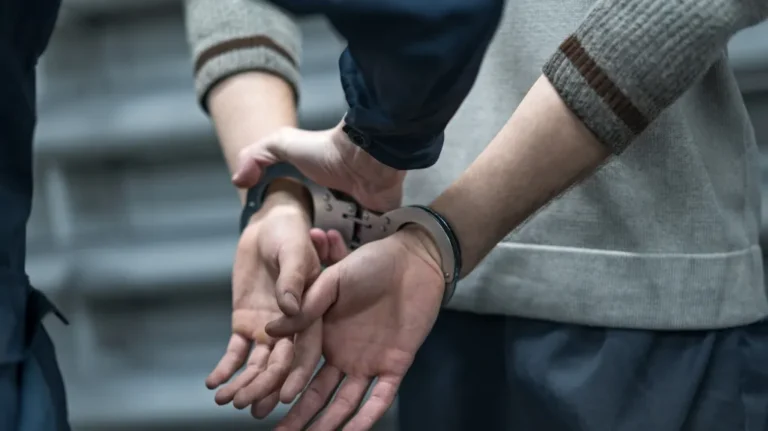 Close-up of a person in handcuffs being restrained by an officer in navy blue uniform.