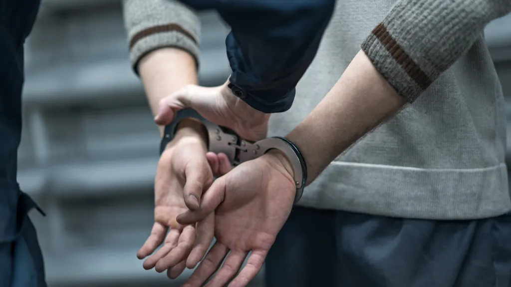 Close-up of a person in handcuffs being restrained by an officer in navy blue uniform.