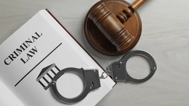 Open book titled "Criminal Law" with metal handcuffs and wooden judge's gavel on a gray surface.